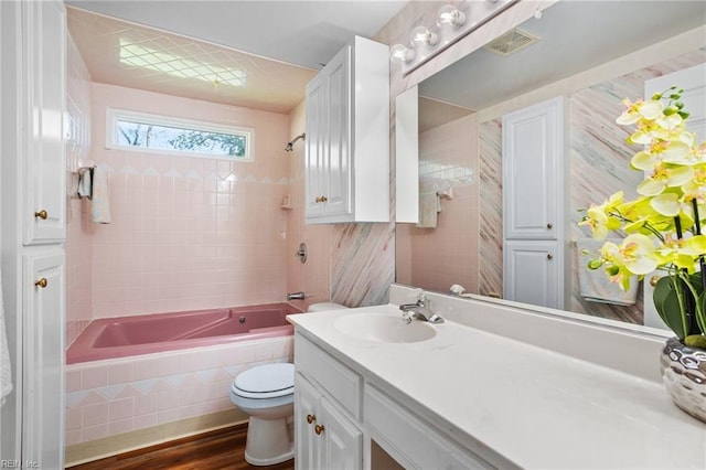 bathroom featuring vanity, tiled shower / bath combo, toilet, and wood finished floors