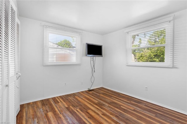 unfurnished bedroom featuring multiple windows, wood finished floors, baseboards, and a closet