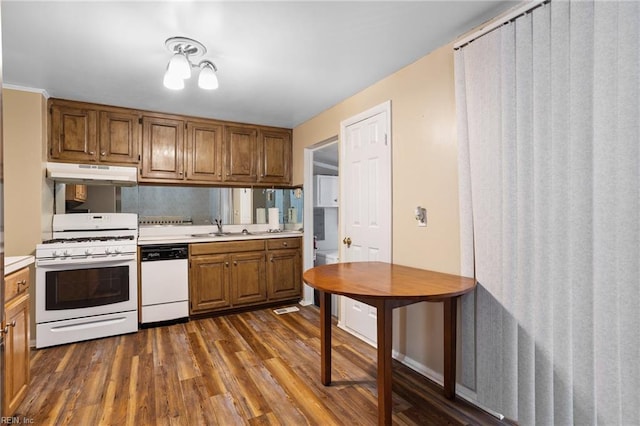 kitchen with white appliances, under cabinet range hood, a sink, light countertops, and dark wood-type flooring