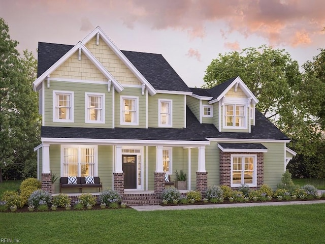 craftsman house featuring a shingled roof, a porch, brick siding, and a front yard