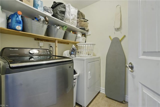 clothes washing area featuring washer and clothes dryer, laundry area, light tile patterned flooring, and baseboards