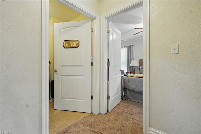 corridor featuring light colored carpet, a textured wall, and light tile patterned floors