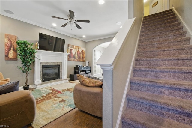 living area featuring wood finished floors, a ceiling fan, a fireplace, ornamental molding, and stairs