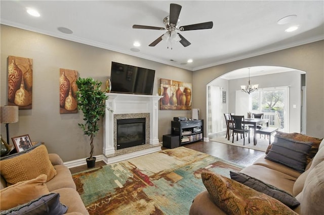 living area with ceiling fan with notable chandelier, a high end fireplace, wood finished floors, ornamental molding, and arched walkways