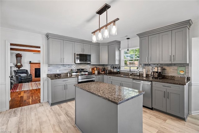 kitchen featuring appliances with stainless steel finishes, gray cabinets, a sink, dark stone countertops, and decorative backsplash