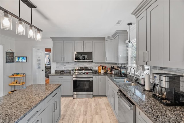 kitchen with appliances with stainless steel finishes, a sink, gray cabinetry, tasteful backsplash, and ornamental molding