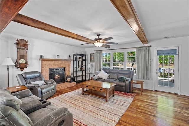 living area with plenty of natural light, wood finished floors, beam ceiling, ceiling fan, and a brick fireplace