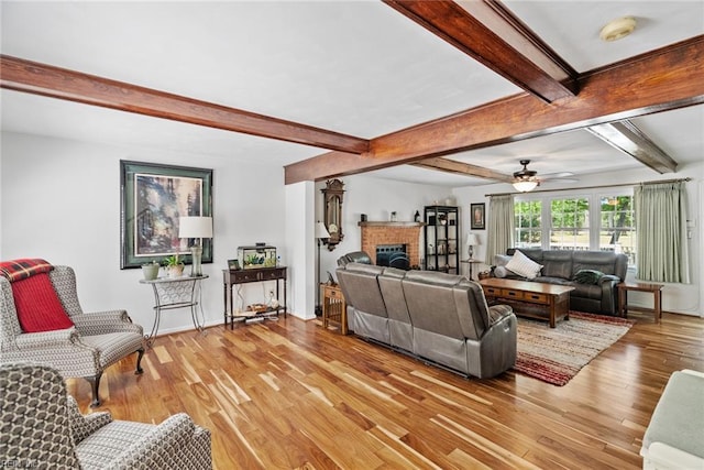 living room featuring light wood-style flooring, beam ceiling, a brick fireplace, and a ceiling fan