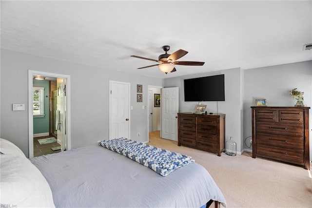 bedroom featuring baseboards, a ceiling fan, light colored carpet, and ensuite bath