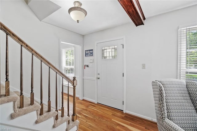 entrance foyer with plenty of natural light, light wood-style floors, beam ceiling, and stairs