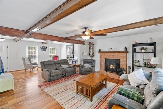 living area with light wood-type flooring, ceiling fan, beamed ceiling, a fireplace, and baseboards