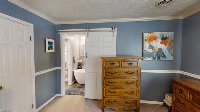 bedroom featuring a textured ceiling, a barn door, baseboards, and ensuite bathroom