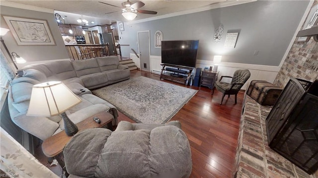 living area with ornamental molding, wood finished floors, ceiling fan, and wainscoting