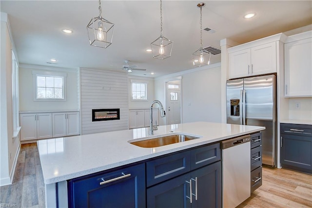 kitchen featuring a ceiling fan, light wood finished floors, a sink, stainless steel appliances, and a fireplace