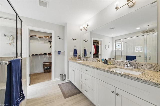 bathroom featuring a shower stall, double vanity, and a spacious closet