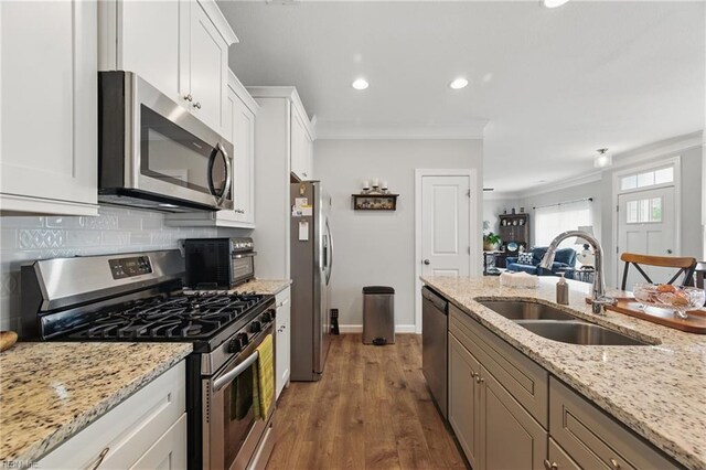 kitchen featuring stainless steel appliances, a sink, ornamental molding, white cabinets, and backsplash