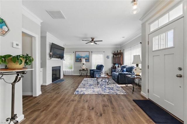 foyer with crown molding, a fireplace, ceiling fan, baseboards, and wood finished floors