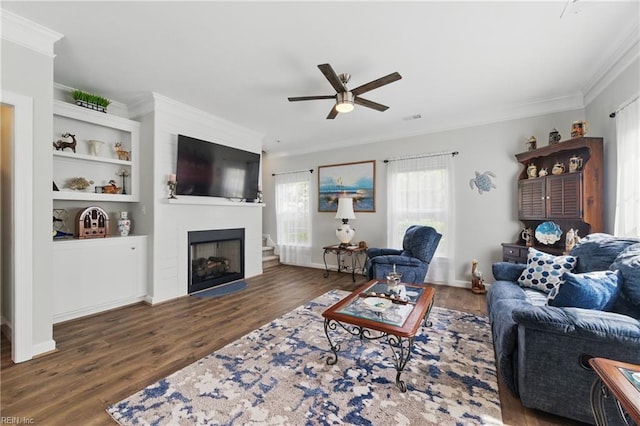 living area featuring ceiling fan, ornamental molding, wood finished floors, a large fireplace, and baseboards