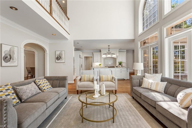 living room featuring a towering ceiling, crown molding, light wood finished floors, arched walkways, and recessed lighting