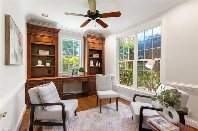 sitting room with healthy amount of natural light, ornamental molding, wood finished floors, a ceiling fan, and baseboards