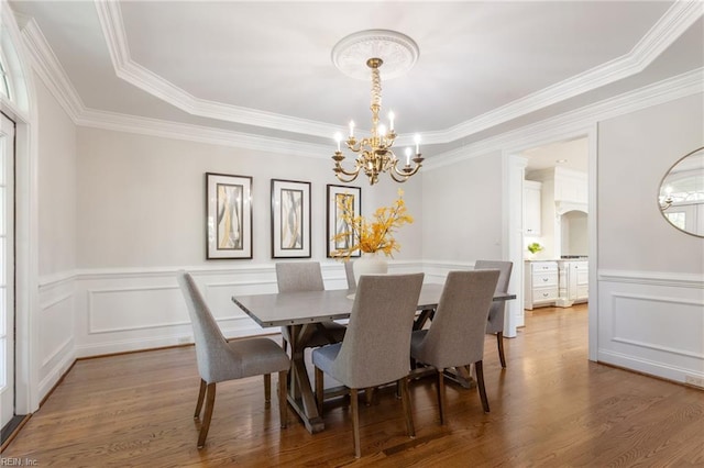 dining area with a chandelier, crown molding, wood finished floors, wainscoting, and a decorative wall