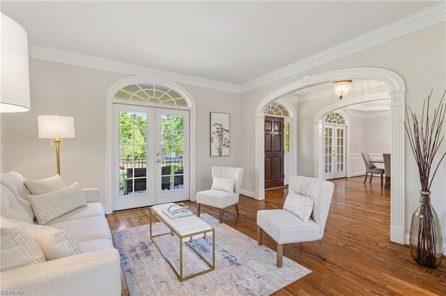 living room with french doors, arched walkways, crown molding, wood finished floors, and baseboards