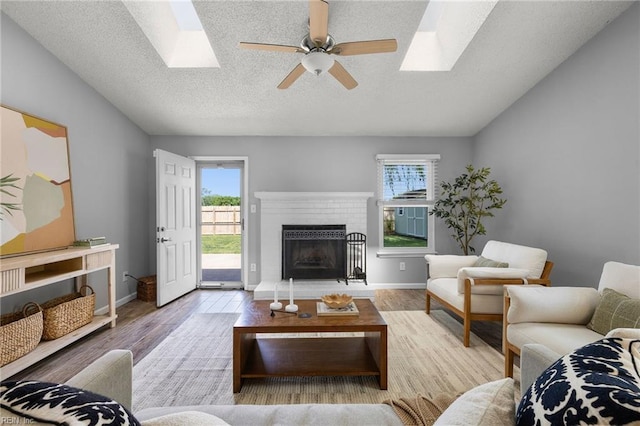 living area featuring a skylight, healthy amount of natural light, ceiling fan, wood finished floors, and lofted ceiling