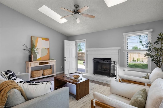 living area featuring a skylight, light wood-style flooring, ceiling fan, plenty of natural light, and a textured ceiling