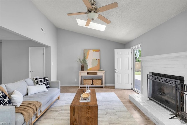 living room featuring lofted ceiling, a ceiling fan, a textured ceiling, a brick fireplace, and light wood-style flooring