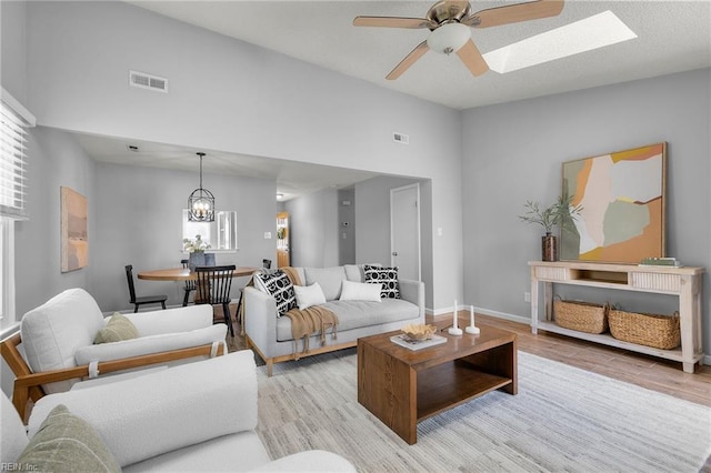 living room featuring wood finished floors, a ceiling fan, a chandelier, a skylight, and baseboards