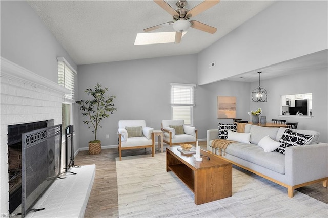 living area featuring lofted ceiling, light wood-type flooring, ceiling fan, a brick fireplace, and baseboards