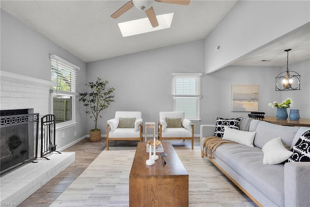 living area featuring lofted ceiling, a skylight, ceiling fan, wood finished floors, and a brick fireplace