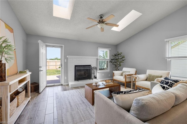 living room with a skylight, lofted ceiling, a brick fireplace, wood finished floors, and a ceiling fan