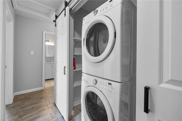 clothes washing area with estacked washer and dryer, wood finished floors, baseboards, and a barn door