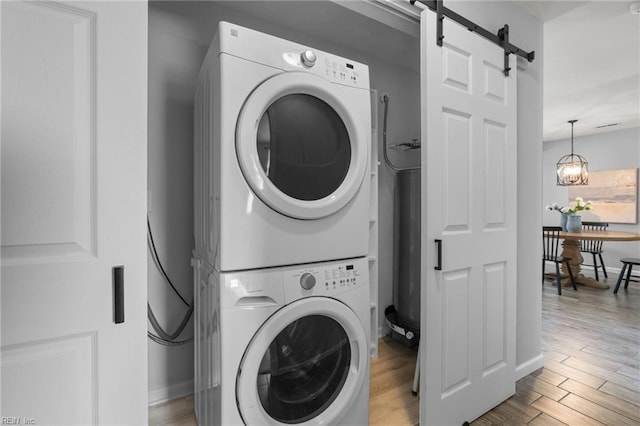 washroom with estacked washer and dryer, a barn door, wood finished floors, and baseboards