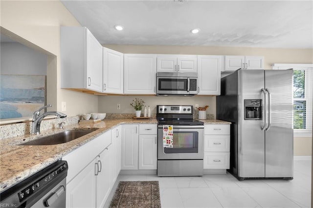 kitchen featuring stainless steel appliances, a sink, white cabinets, light stone countertops, and recessed lighting
