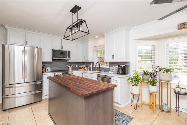 kitchen featuring appliances with stainless steel finishes, wood counters, a sink, light tile patterned flooring, and ornamental molding