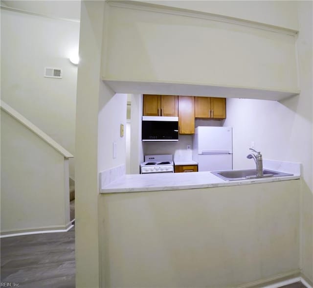 kitchen with white appliances, a sink, a peninsula, dark wood-type flooring, and baseboards