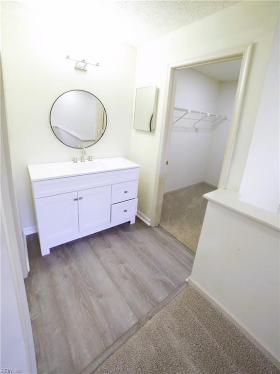 bathroom with vanity, wood finished floors, a spacious closet, and baseboards