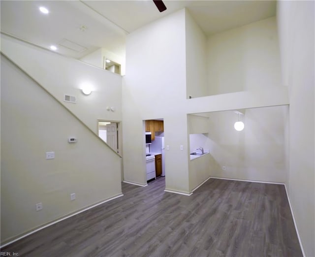 unfurnished living room with wood finished floors, baseboards, a towering ceiling, and a ceiling fan