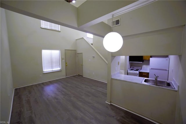 unfurnished living room featuring a sink, dark wood finished floors, a high ceiling, and baseboards