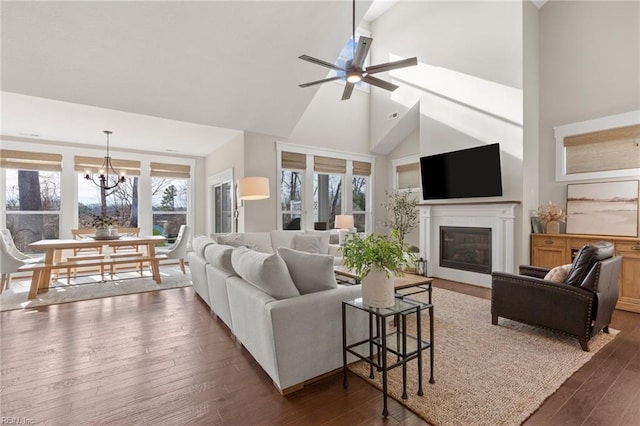 living room with high vaulted ceiling, a chandelier, a ceiling fan, a glass covered fireplace, and wood finished floors