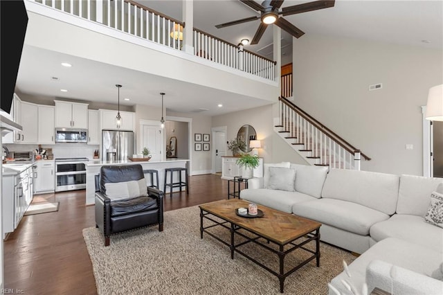 living room featuring a towering ceiling, a ceiling fan, dark wood-style flooring, recessed lighting, and stairs