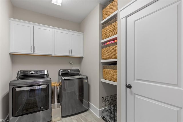 clothes washing area with washing machine and clothes dryer, cabinet space, baseboards, and light wood-type flooring