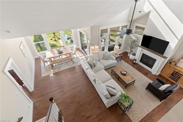 living area featuring wood finished floors, a ceiling fan, healthy amount of natural light, a glass covered fireplace, and lofted ceiling