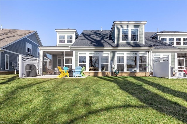 rear view of house featuring a sunroom, a lawn, and a shingled roof