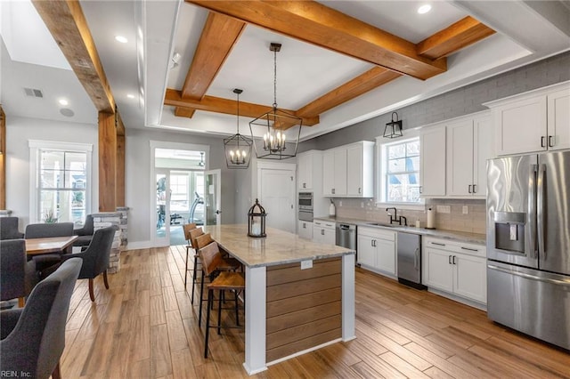 kitchen with appliances with stainless steel finishes, light wood finished floors, tasteful backsplash, a breakfast bar, and plenty of natural light