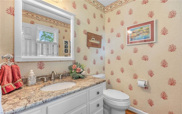 half bathroom featuring toilet, wallpapered walls, and vanity