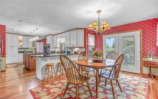 dining space featuring a chandelier, wallpapered walls, light wood-style flooring, and french doors