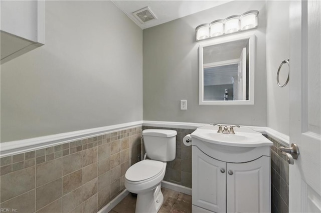 half bathroom featuring toilet, tile walls, wainscoting, and vanity